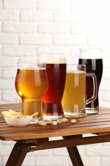 Glasses with different types of beer and snacks on wooden table