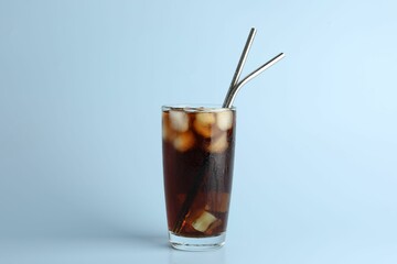 Tasty refreshing drink with straws in glass on light blue background