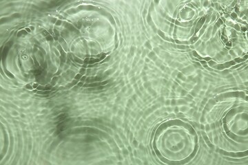 Rippled surface of clear water on light green background, top view