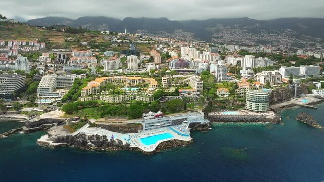 Aerial drone view of Funchal city with hotels resorts and swimming pool along the coast of Atlantic ocean. Funchal, Madeira, Portugal. Orbit parallax shot