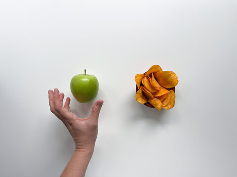 Woman chooses a green apple over unhealthy potato chips. Hand reaches out to healthy fruit instead of snacks.