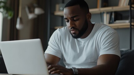 Obraz premium African American man sitting at home filling out an online survey on his laptop, giving feedback and completing a checklist.