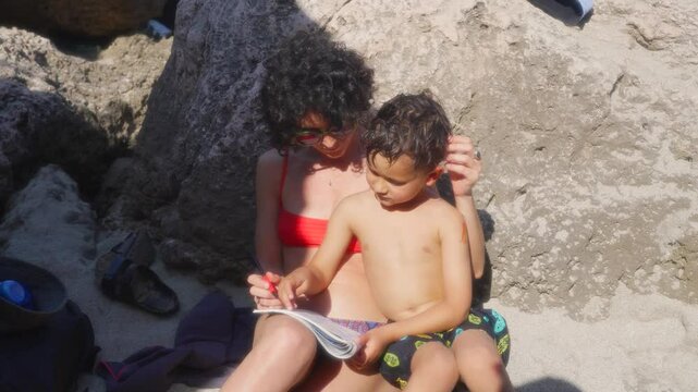 A mum shares and teaches her child arrowwords on the beach, in France