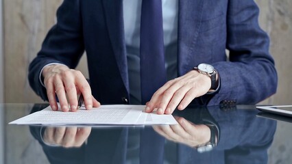 Businessman reviewing documents at office desk. Close-up of a professional man's hands examining paperwork with pen and tablet in sight. Business people concept