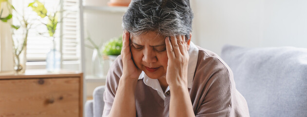 Elderly women feeling dizzy and headache sit on the sofa at home.