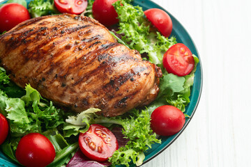Grilled chicken breast ( fillet ) with lattuce salad and cherry tomatoes . Top view