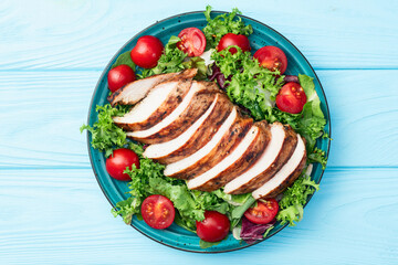 Grilled chicken breast ( fillet ) with lattuce salad and cherry tomatoes . Top view