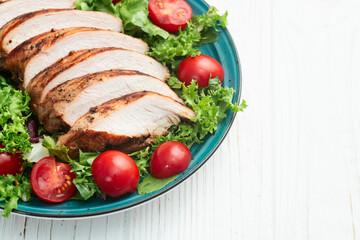 Grilled chicken breast ( fillet ) with lattuce salad and cherry tomatoes . Top view