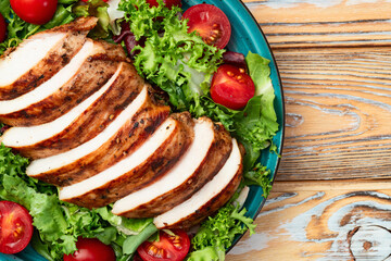 Grilled chicken breast ( fillet ) with lattuce salad and cherry tomatoes . Top view
