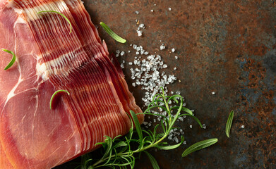 Sliced prosciutto and rosemary on a brown rusty background.