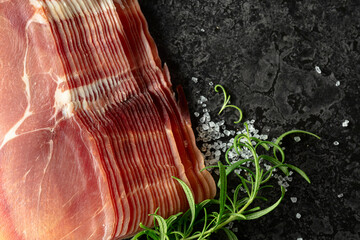 Sliced prosciutto and rosemary on a stone table.