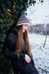 a beautiful young girl with long blond hair in a hat and a long down jacket plays with snow and enjoys winter nature