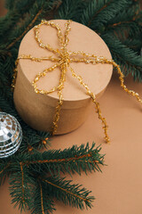 Christmas, festive background. Brown gift box with goolden ribon on green coniferous branches on a brown background. Top view
