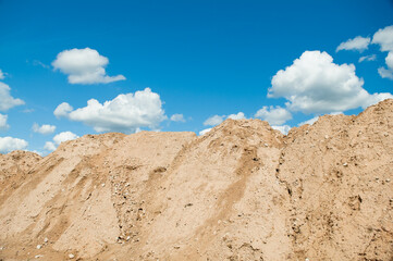 a mountain of sand against a blue sky and clouds