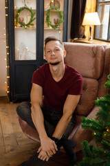 young man relaxing in an armchair near a decorated Christmas tree with warm lights in a cozy room during the holiday season