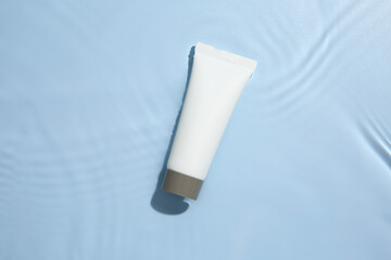 Cosmetic product. Tube with cream in water on light blue background, top view