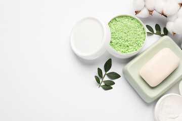 Different cosmetic products, cotton flowers and green leaves on white background, flat lay. Space for text