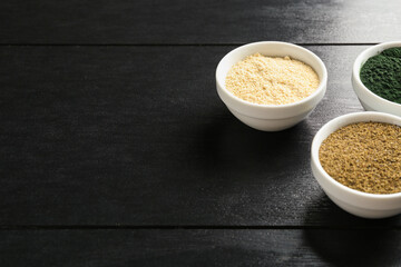 Different healthy superfoods in bowls on black wooden table, space for text