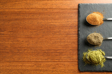 Different superfood powders in spoons on wooden table, top view. Space for text