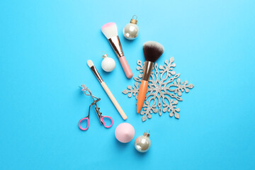 Makeup brushes, eyelash curler and Christmas decor on light blue background, flat lay