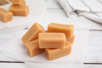 Tasty sweet caramel candies on white wooden table, closeup