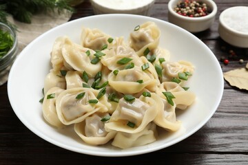 Delicious pelmeni with green onion served on wooden table, closeup