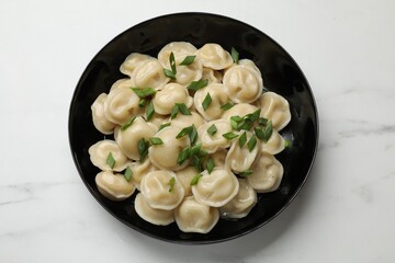 Delicious pelmeni with green onion in bowl on light table, top view