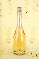 Shiny confetti, streamers and sparkling wine on beige background