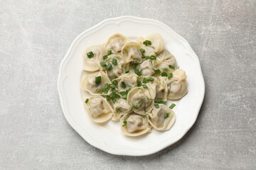 Delicious pelmeni with green onion and dill on grey textured table, top view