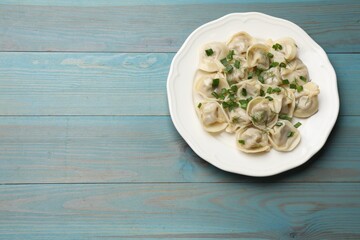 Delicious pelmeni with green onion and dill on blue wooden table, top view. Space for text