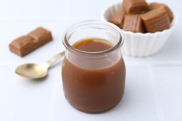 Tasty caramel sauce in jar on white table, closeup