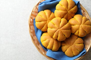 Wicker basket with tasty pumpkin shaped buns on light table, top view. Space for text