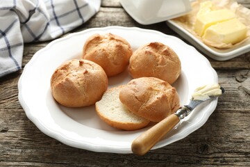 Plate with homemade tasty buns, butter and knife on wooden table, closeup