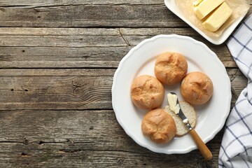 Plate with homemade tasty buns, butter and knife on wooden table, flat lay. Space for text