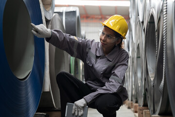 Metalwork manufacturing, warehouse of raw materials. Woman factory worker inspecting quality rolls of galvanized or metal sheet. Woman worker working in warehouse of rolls stainless steel