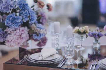 Flowers and candles on table. blue and white flowers decorate the table. Beautiful table set with glasses, plates, candles and flowers for a festive event, party or wedding reception.