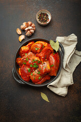 Raw uncooked chopped pieces of meat marinated with seasonings and parsley in black casserole dish top view on dark rustic background. Cooking ragout stew with marinated meat fillet pieces.