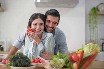 Happy couple preparing food at home, various fresh vegetable salad on counter in kitchen