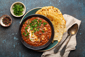 Traditional Indian Punjabi dish Dal makhani with lentils and beans in black bowl served with naan...