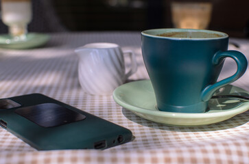 a sea-green coffee cup, a white milk jug and a smartphone on the table in the cafe