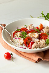 bowl of salad with rice, cod liver and cherry tomatoes on light table