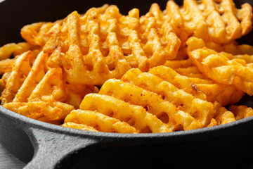 Waffle criss cross fries in a cast iron frying pan on a wooden cutting board. Unhealthy fast food concept