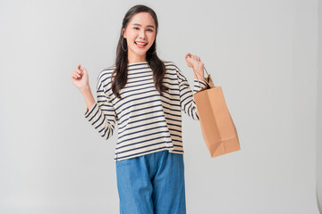 Happy woman holding shopping bag, wearing striped shirt and blue pants, celebrating her purchase with joy and excitement