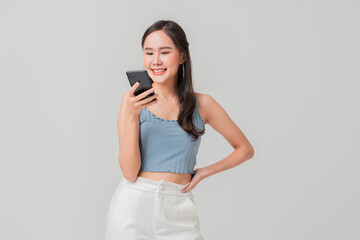Fototapeta premium A young woman smiles while using her smartphone, showcasing casual and cheerful vibe. Her stylish outfit complements modern setting