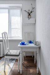  nice cozy white kitchen. Wooden table and chair, bright blue glass dishes on the table. Beautiful kitchen