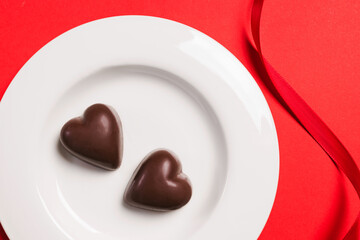 Delicious heart-shaped chocolates on a white plate on a red background for Valentine's day