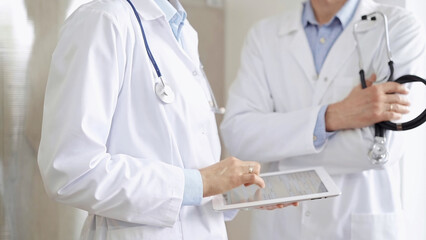 Two doctors wearing white coats and stethoscopes, using a digital tablet, discussing a patient's medical history. Medicine and science