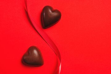 Delicious heart-shaped chocolates on a red background with a ribbon, Valentine's day celebration