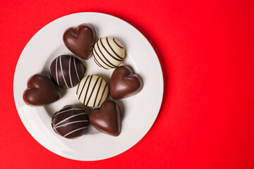 Delicious assorted chocolates on a white plate on red background for Valentine's day celebration