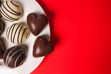 Delicious assorted chocolates on a white plate on red background for Valentine's day celebration